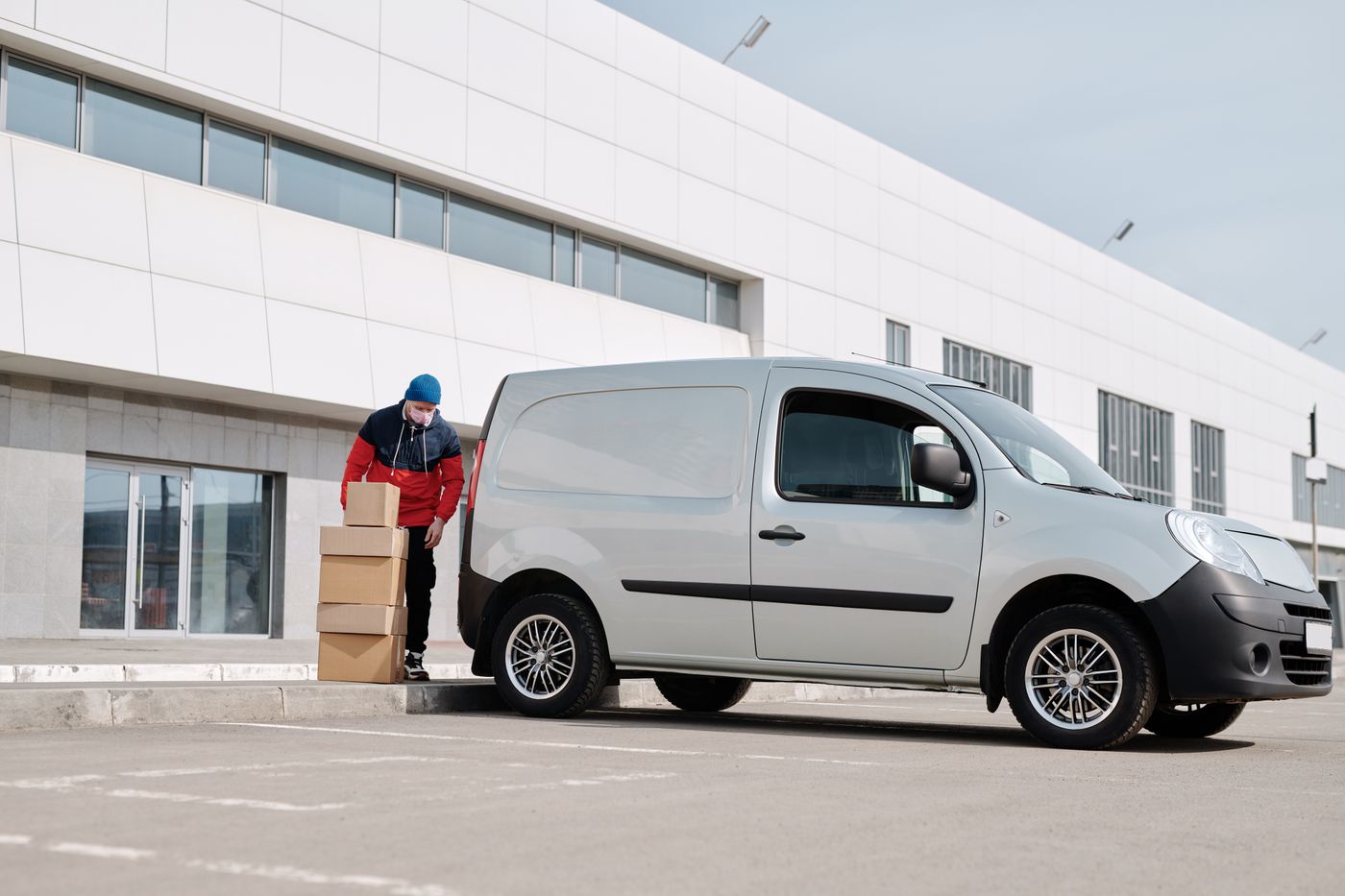 Delivery worker handling cardboard boxes beside a grey van outside a warehouse