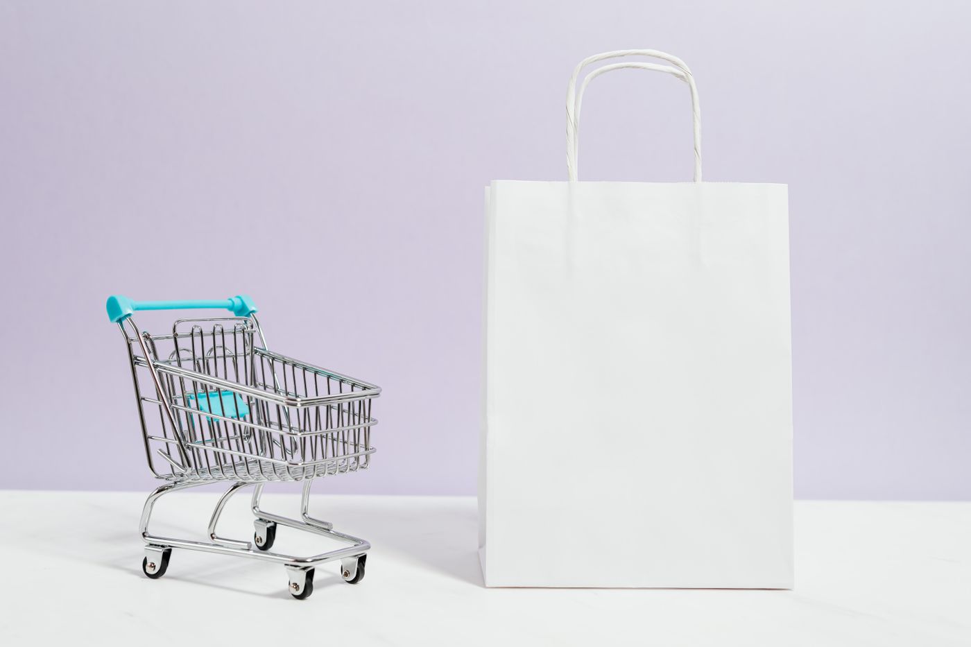 White shopping bag beside a miniature shopping cart on a pale surface