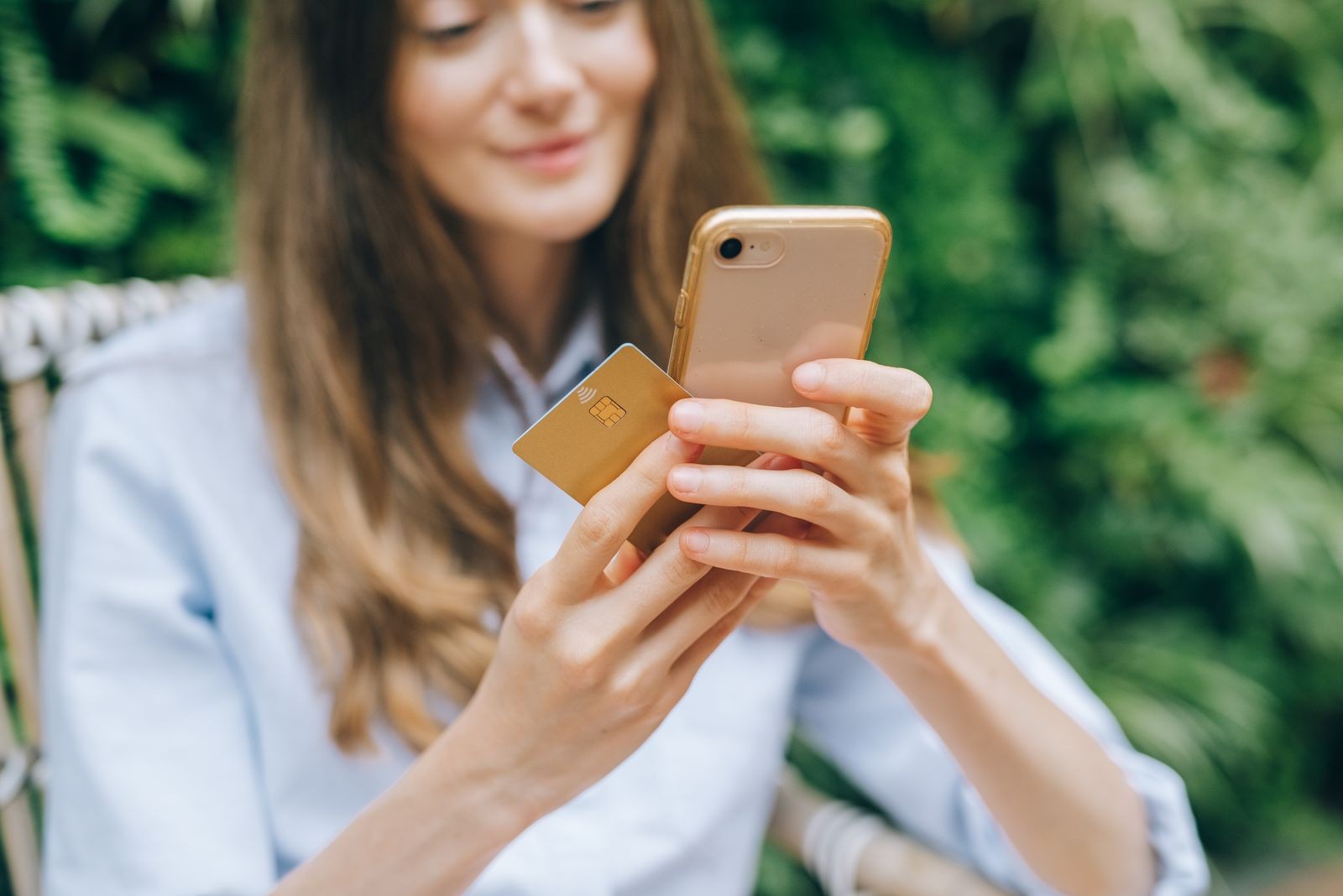 Woman using a smartphone and payment card beside greenery