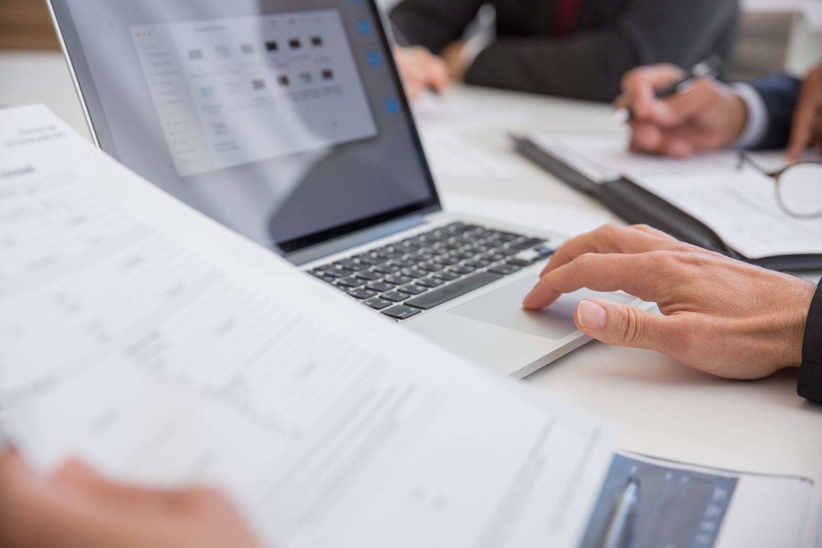 Hands on a laptop beside printed reports at a meeting table