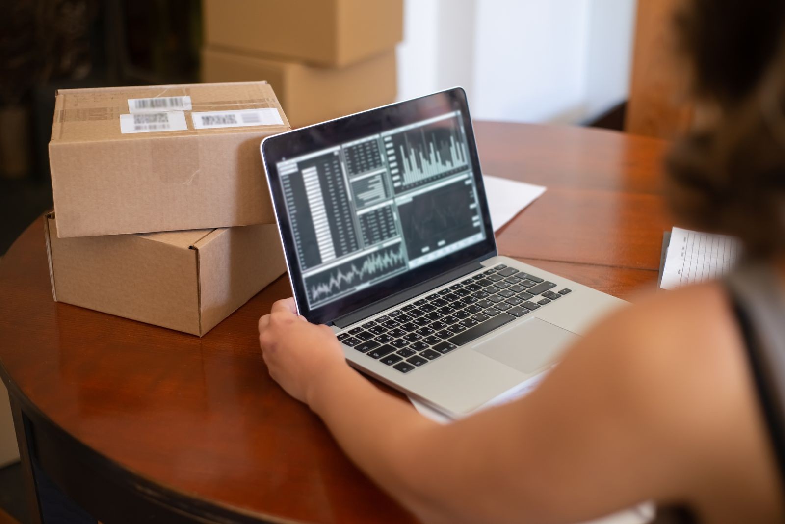 Online seller reviewing sales charts on a laptop beside packed orders